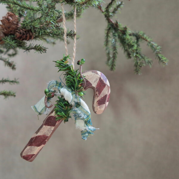 red and white candy cane ornament with green bow and pine