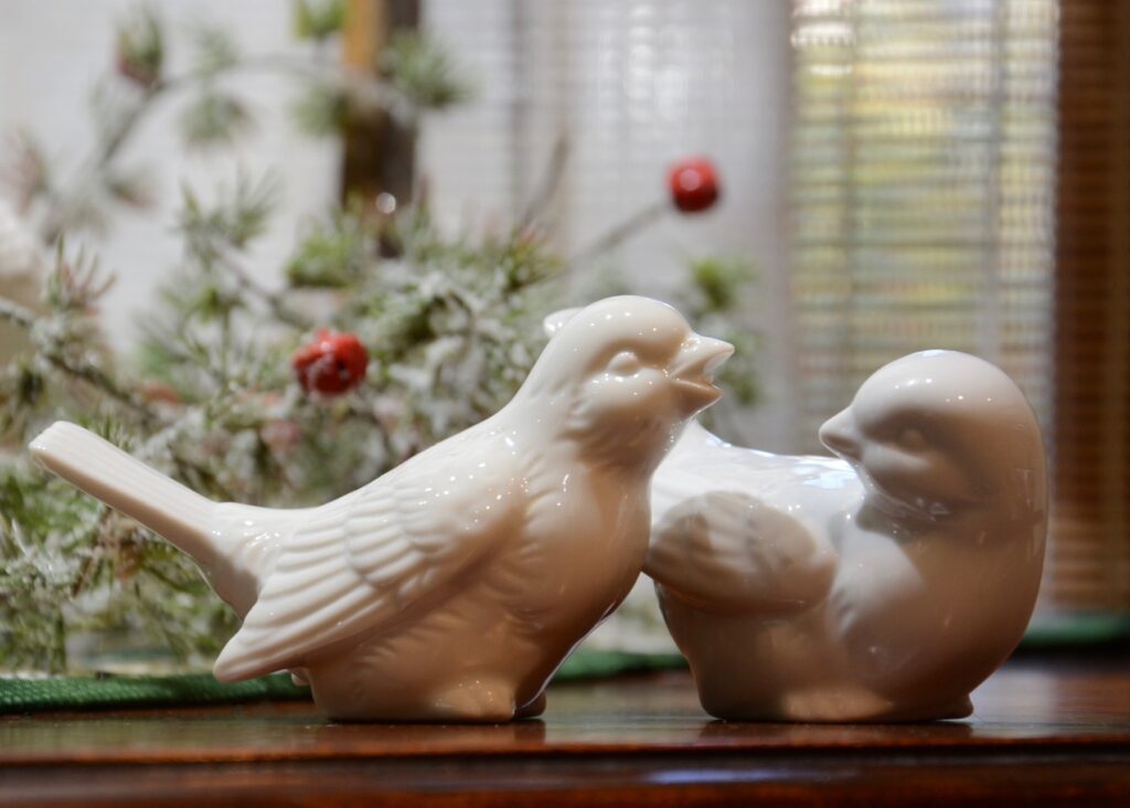 Two porcelain vintage birds with pine and berries garland in background.