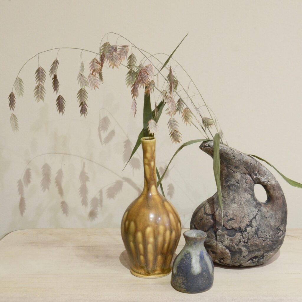 three pieces of pottery with dried grass in one