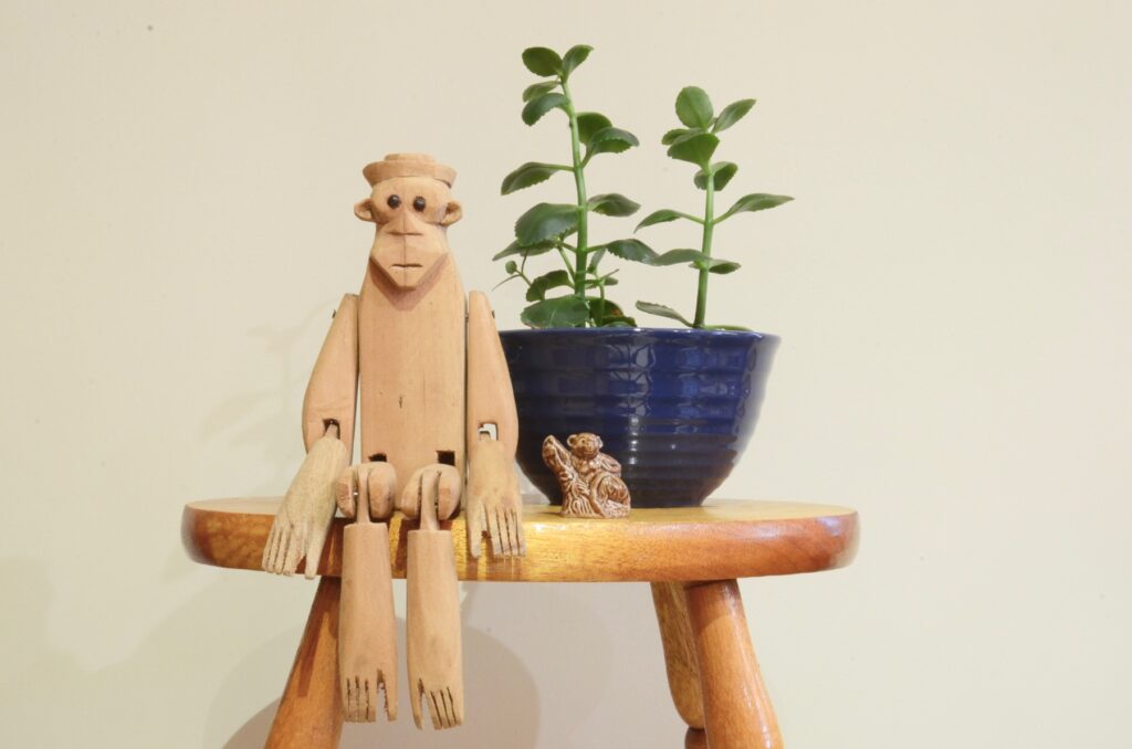 wooden monkey sitting on bench with live plant in blue bowl with ceramic monkey